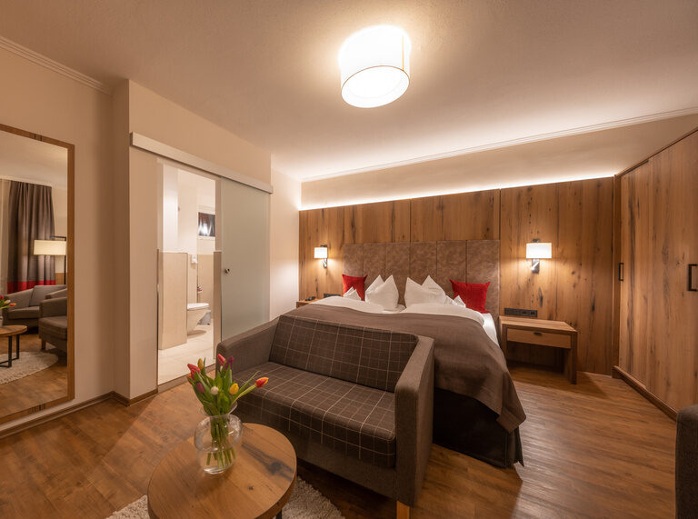 Ein geschmackvoll gestaltetes Doppelzimmer mit Panoramablick und einem Südbalkon mit Bett und Couch im Bayerischen Wald.