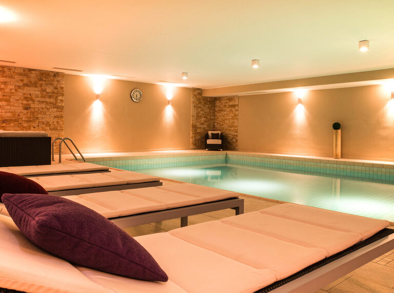 Ein elegantes Hallenbad mit durchdachtem Design und komfortablen Liegestühlen lädt zum Verweilen ein.