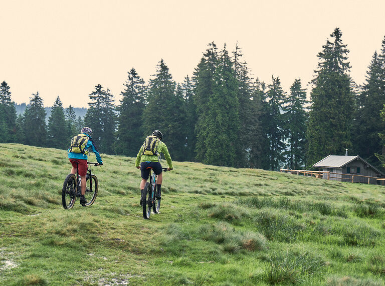 Radfahrer auf dem Weg über ein Feld zu einer Hütte im Bayerischen Wald.