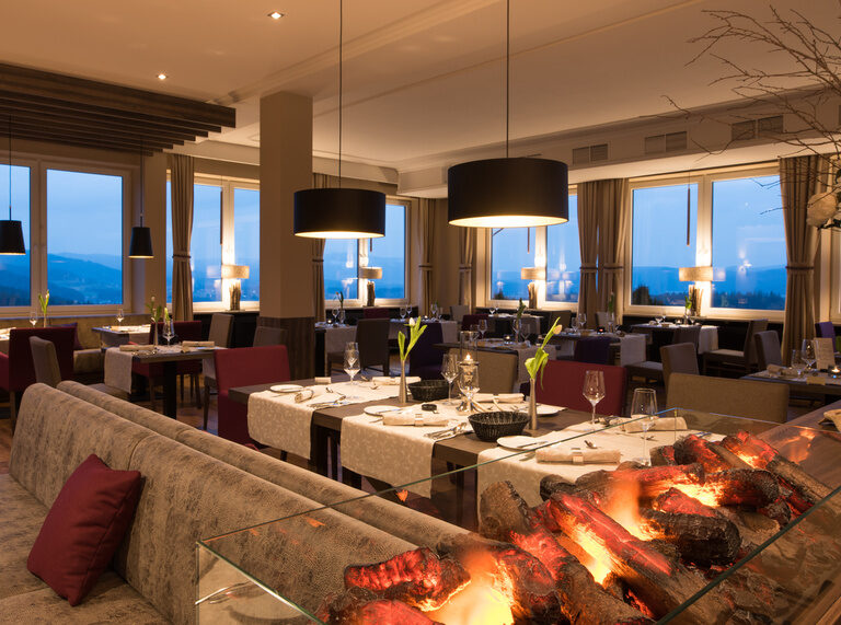 Ein Restaurant mit Tischen und Stühlen vor großen Fenstern.