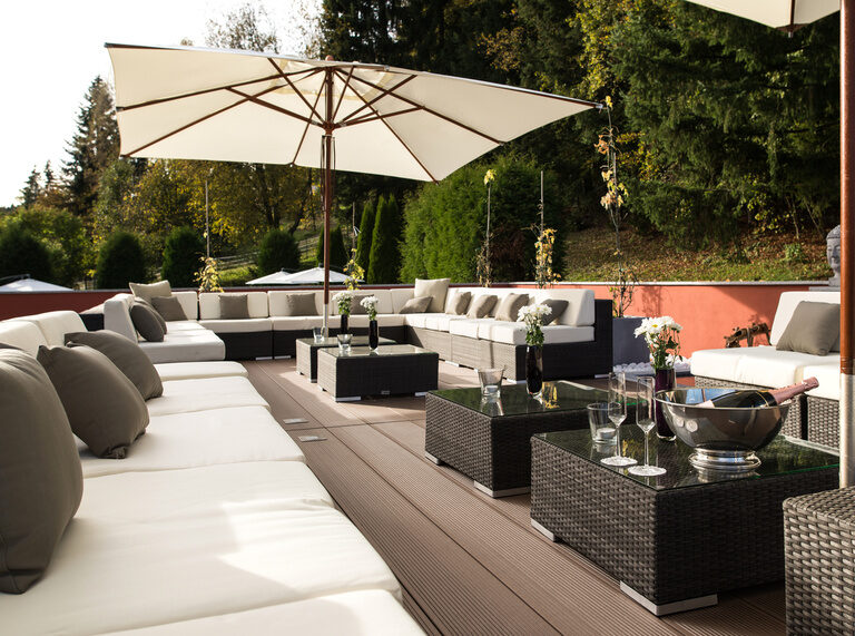 Eine Terrasse mit Outdoor-Tischen und Stühlen unter Sonnenschirmen.