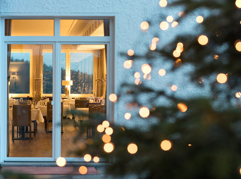 Ein geschmückter Weihnachtsbaum vor dem Haus in der winterlichen Abenddämmerung.